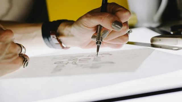 Manos diseñando a lápiz sobre papel albanene el boceto de un logotipo, proceso de diseño de marca