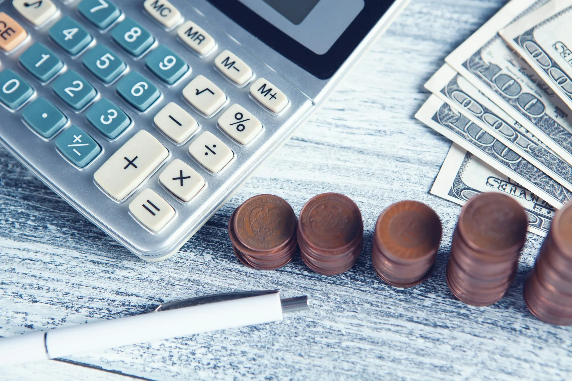 Calculadora, una pluma y billetes sobre una mesa, listos para planear el presupuesto de publicidad de un negocio