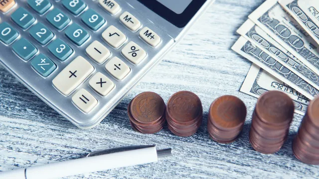 Calculadora, una pluma y billetes sobre una mesa, listos para planear el presupuesto de publicidad de un negocio