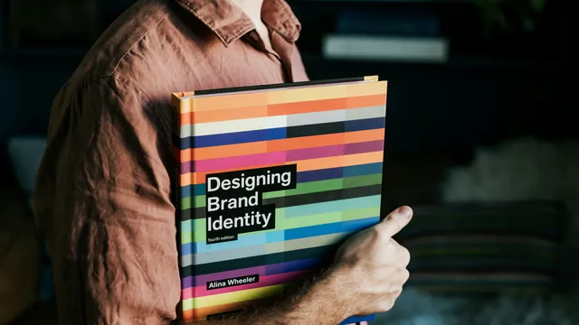 Persona sosteniendo el libro Designing Brand Identity, referencia al manual de marca de una PyME