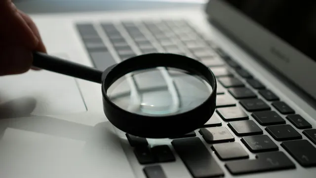 Lupa junto a una laptop gris sobre un escritorio, búsqueda de palabras clave para un negocio local en Guadalajara
