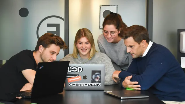 Cuatro personas trabajando juntas alrededor de una laptop, el tamaño de equipo típico de un estudio creativo