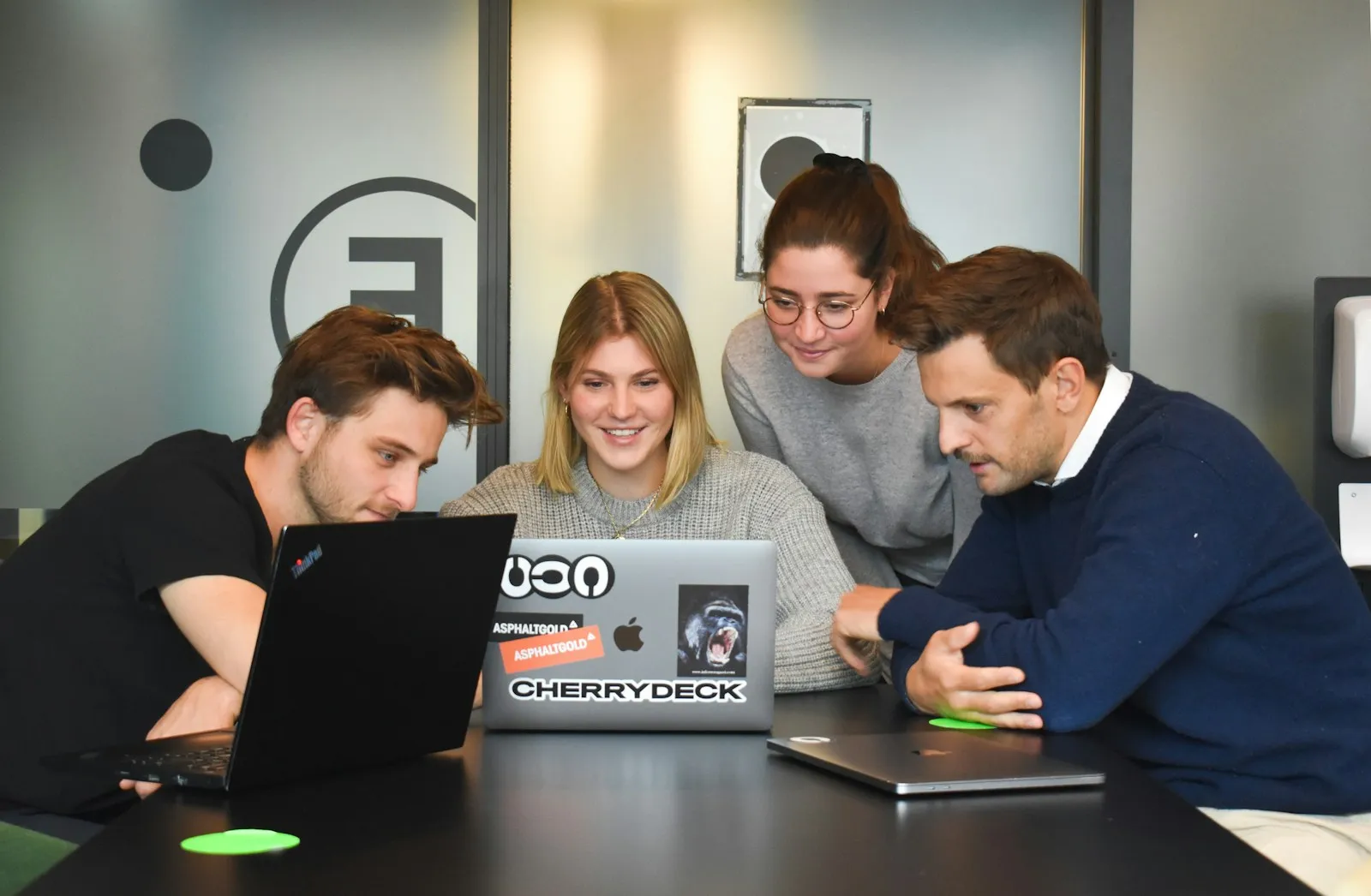 Cuatro personas trabajando juntas alrededor de una laptop, el tamaño de equipo típico de un estudio creativo